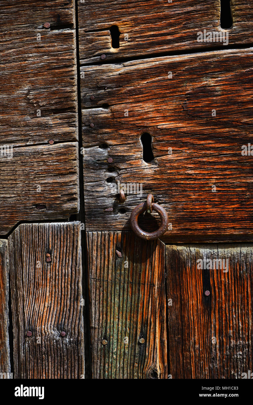 Very old wooden door with worn varnish, many keyholes and rusty iron