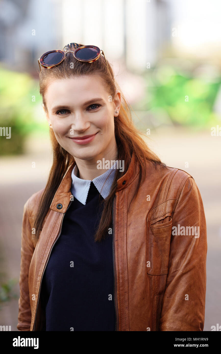 Portrait of pretty smiling girl in brown leather jacket and round sunglasses on her forehead Stock Photo