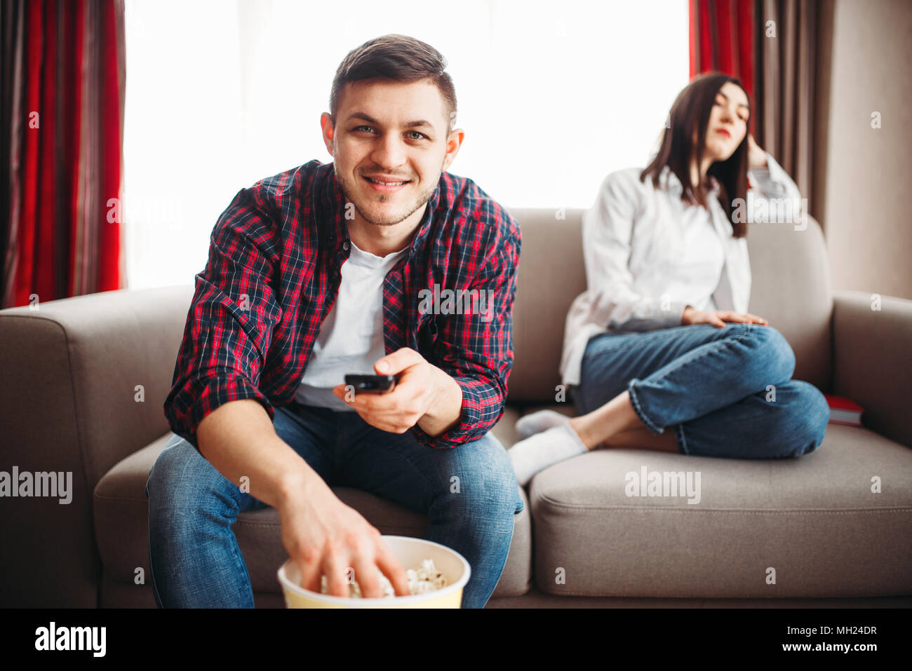 Man watch tv and eats popcorn, woman in a bad mood Stock Photo