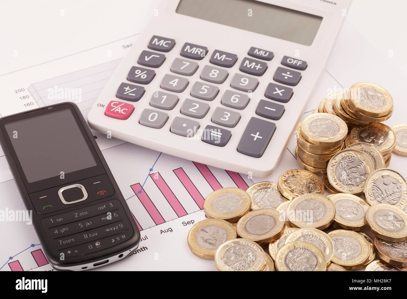 A calculator sitting on some graphs labelled savings and funds with some new (post 2016) pound coins. Stock Photo