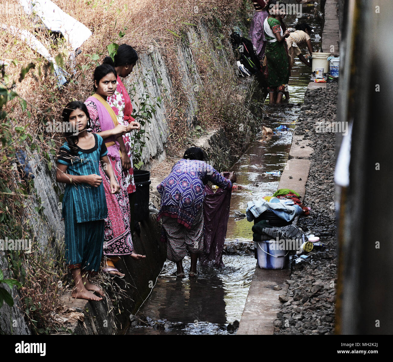 A group of women and girls washing the laundry in a gully full of water right alongside the railway tracks, India Stock Photo