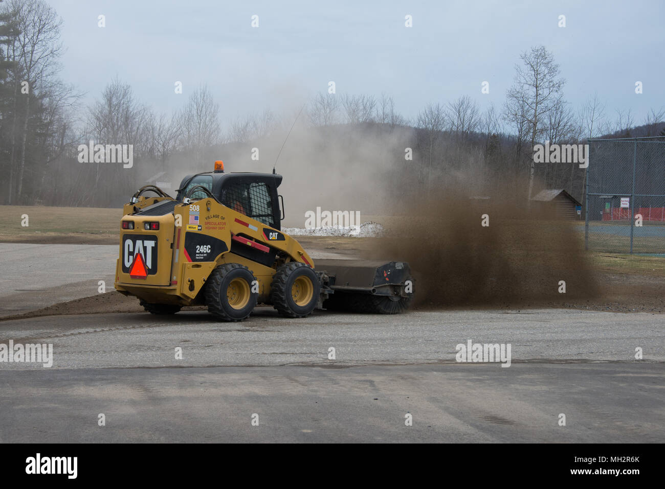 A Caterpillar 246C with a rotary brush sweeping the winters sand and gravel off a parking lot in Speculator, NY USA Stock Photo