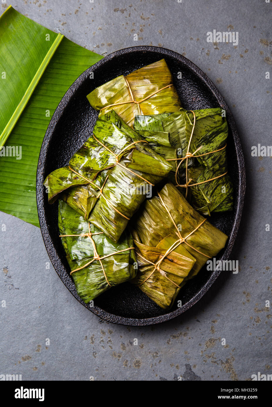 COLOMBIAN, CENTRAL AMERICAN FOOD. Tamales wrapped in banana palm tree leaves on black plate