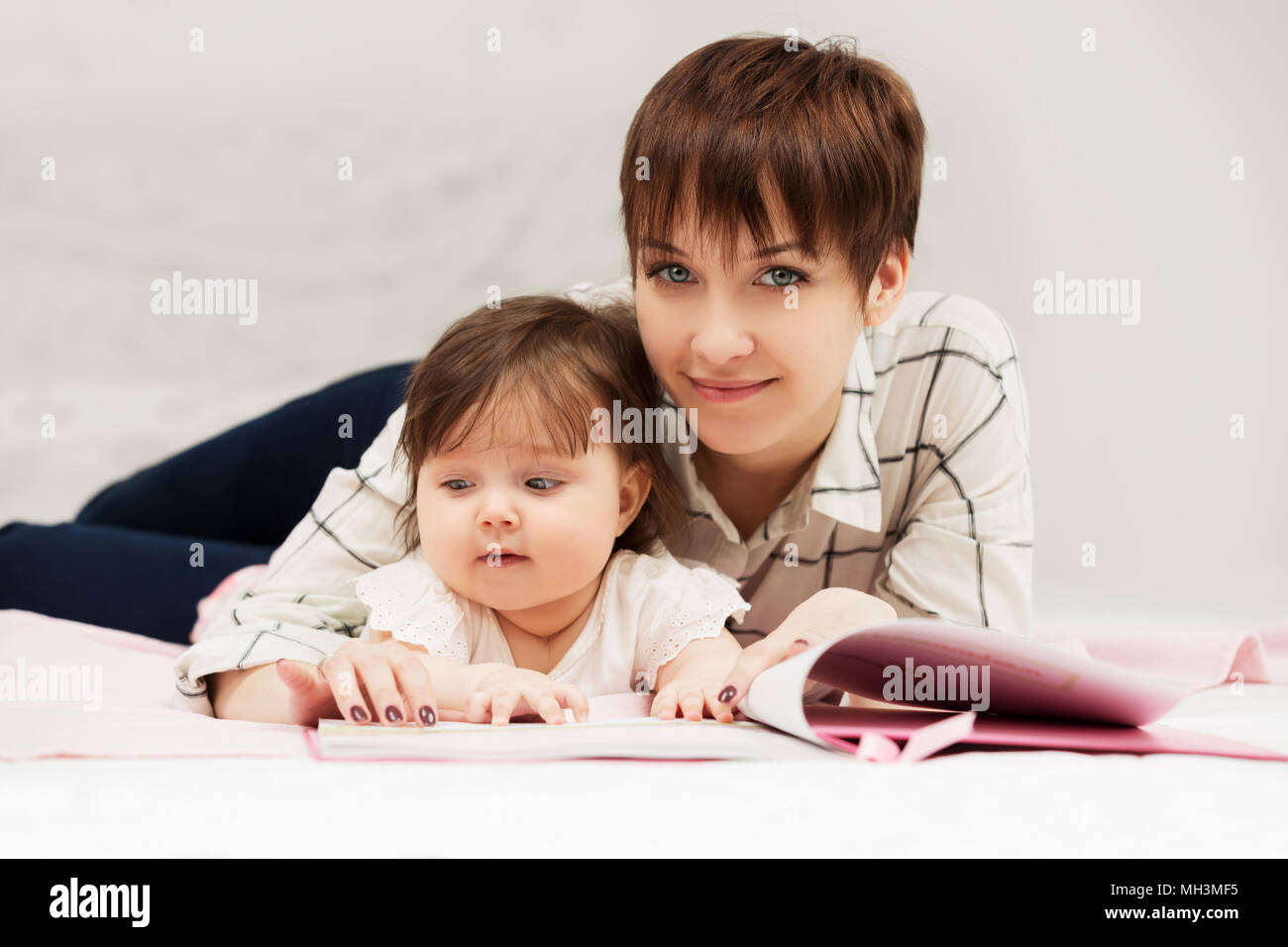Mother and little baby girl reading a book on bed Stock Photo