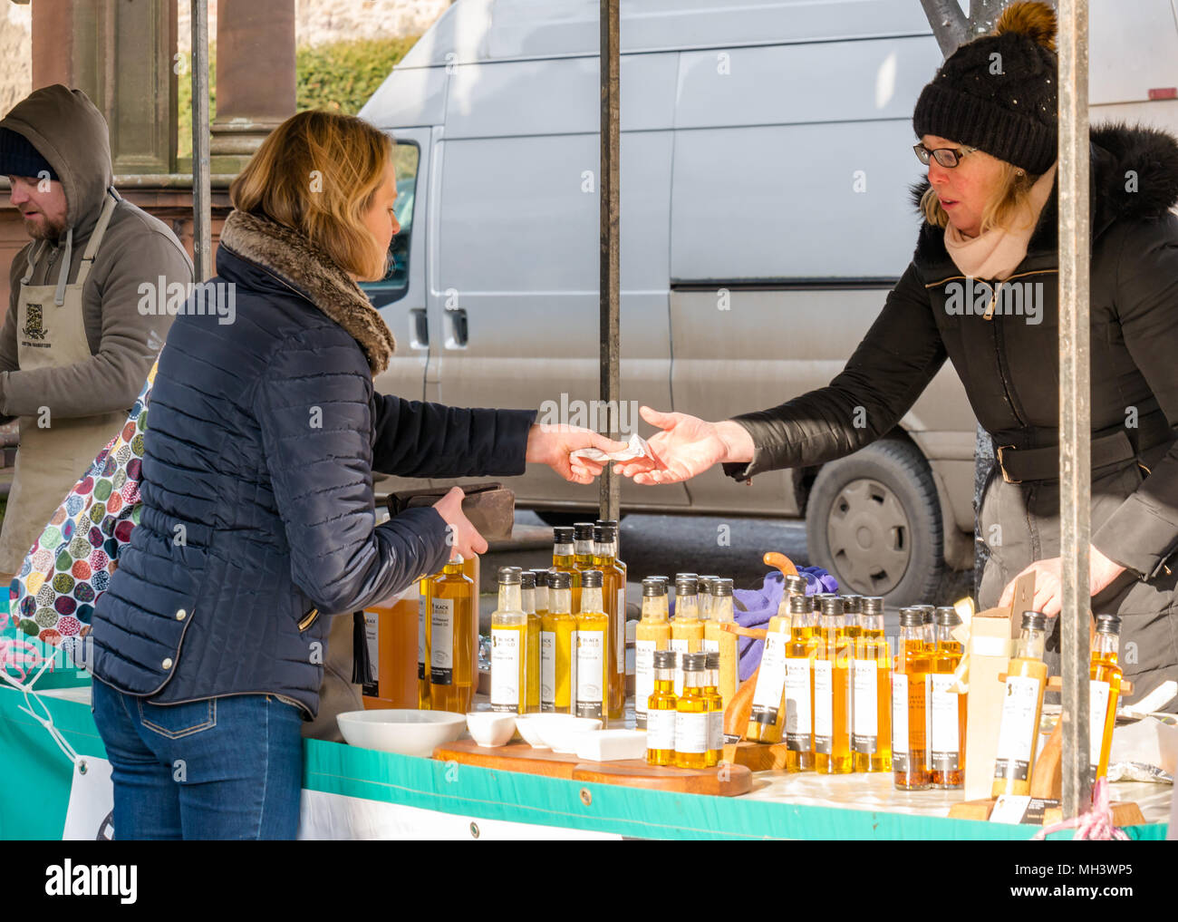 Woman paying at Black & Gold oils outdoor market stall, Haddington Farmers Market, Place d'Aubigny, Court Street, East Lothian, UK on Winter day Stock Photo