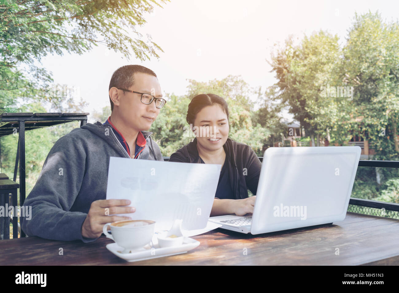 Asia couples middle age freelance holding business chart working with laptop at outdoor restaurant or cafe. Stock Photo