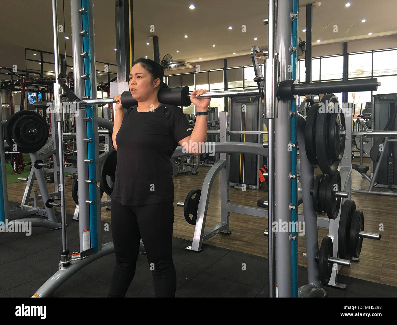 Asia fat girl training squat by barbell equipment in the gym for strength, weight loss. Stock Photo