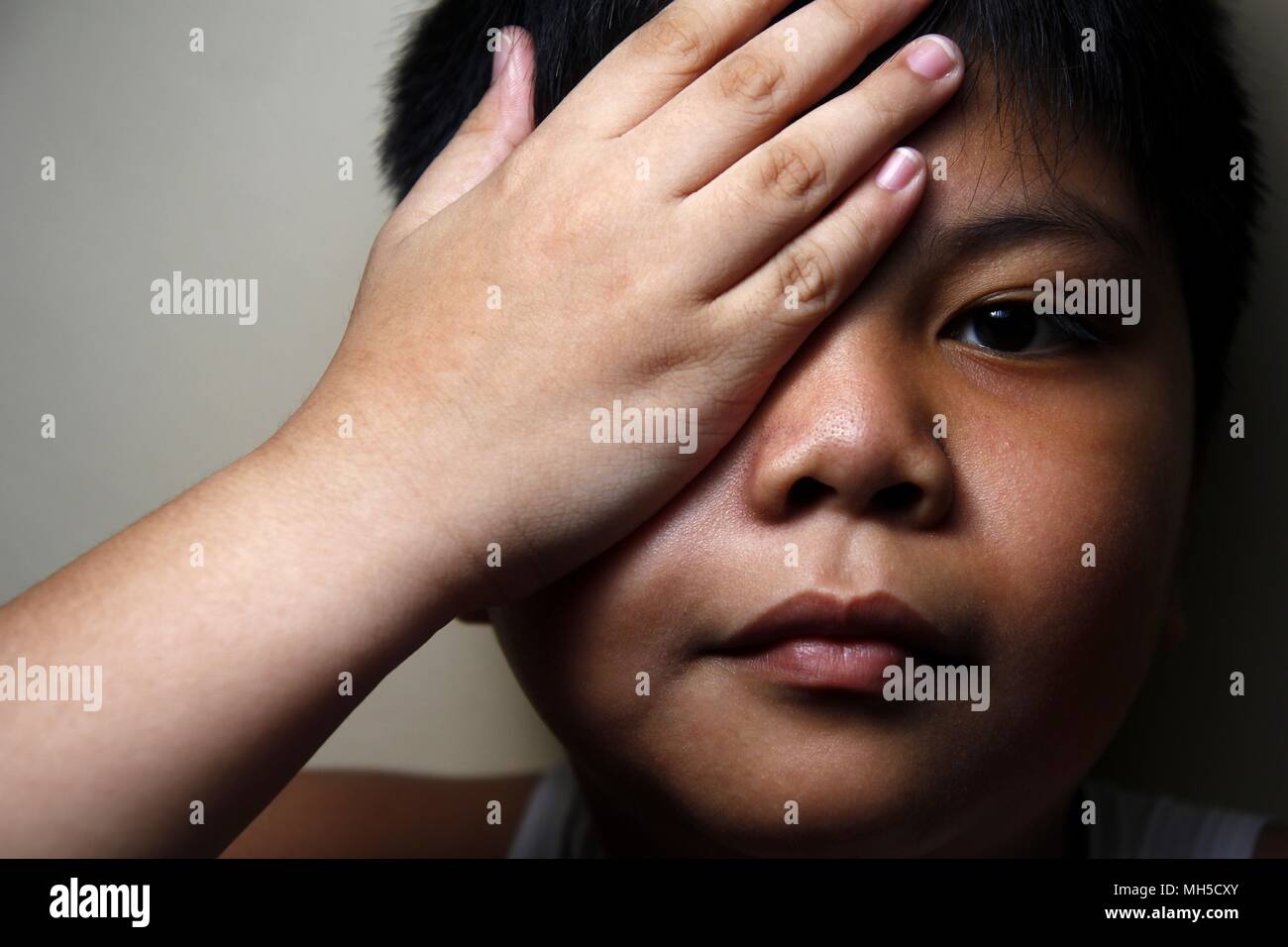 Close up photo of a young Asian boy covering one of his eyes Stock Photo