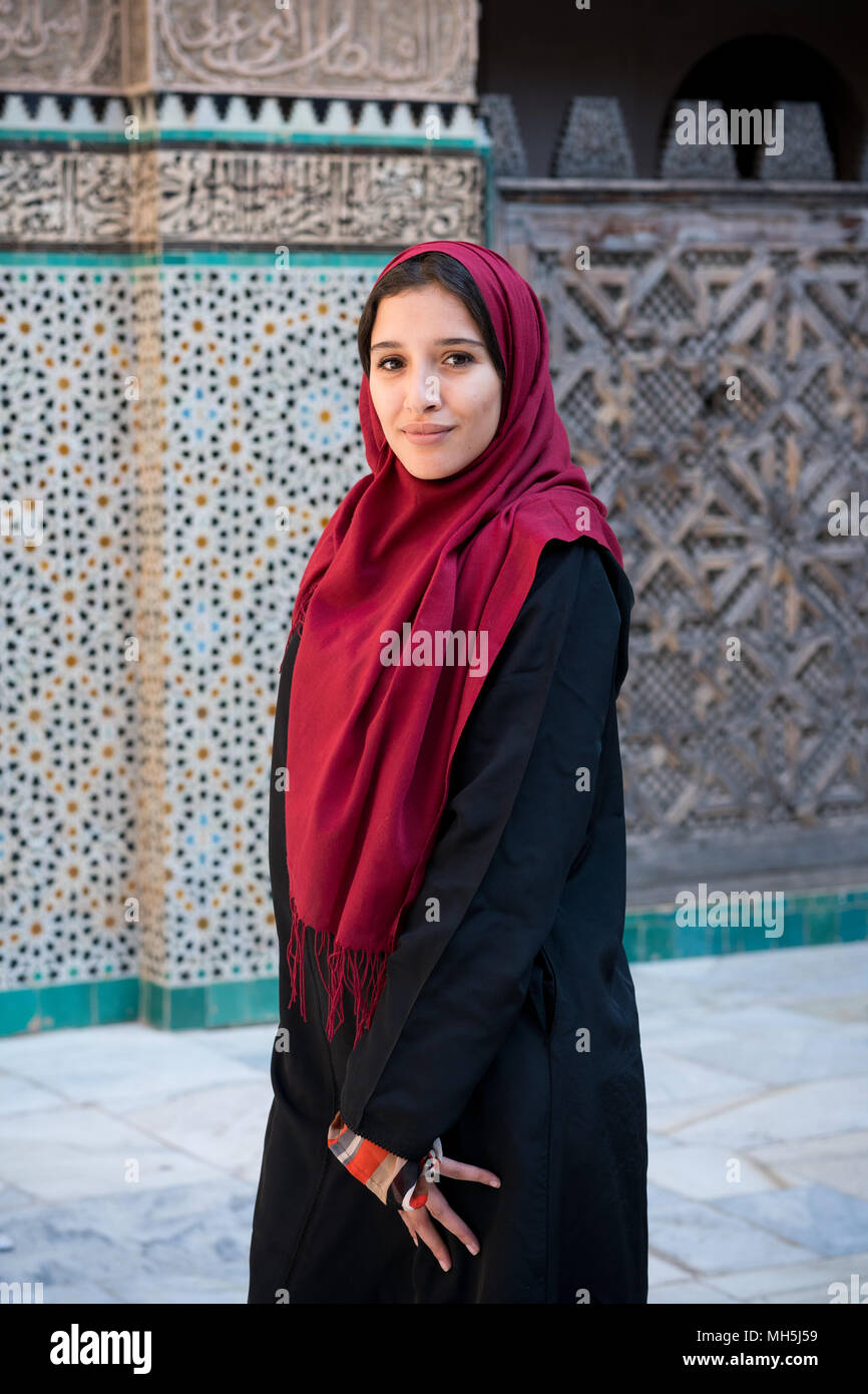 Muslim woman posing in traditional clothing with red hijab and black dress in front of traditional arabesque decorated wall Stock Photo
