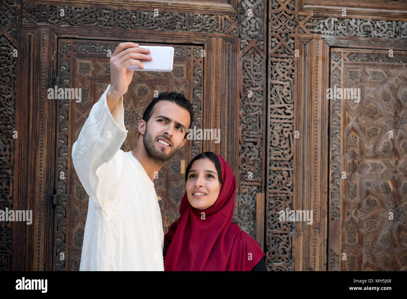 Young Muslim couple smiling and taking selfie with smart phone Stock Photo