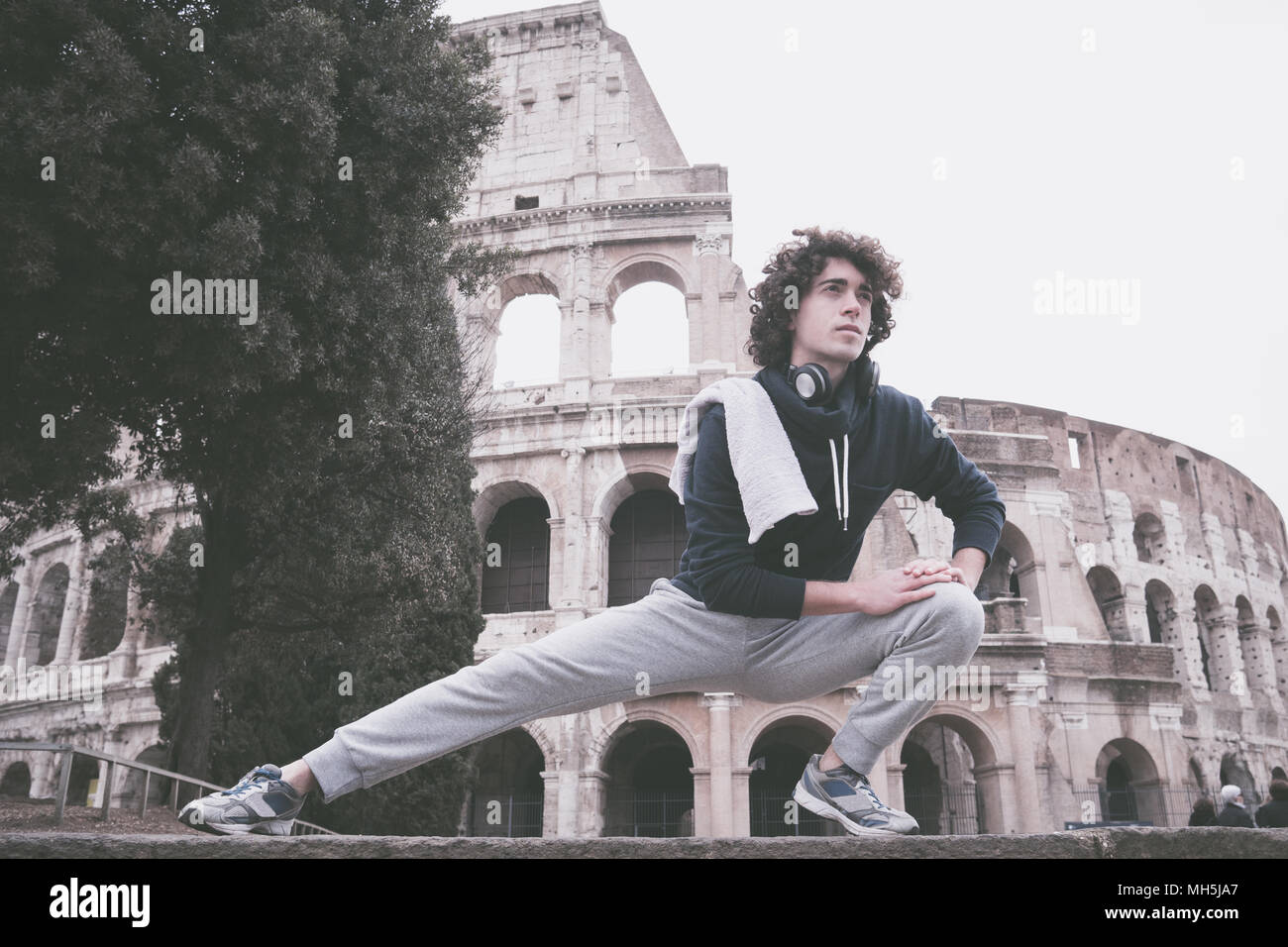 Handsome young sportsman stretching and warming-up for training in front of Colosseum in Rome Stock Photo