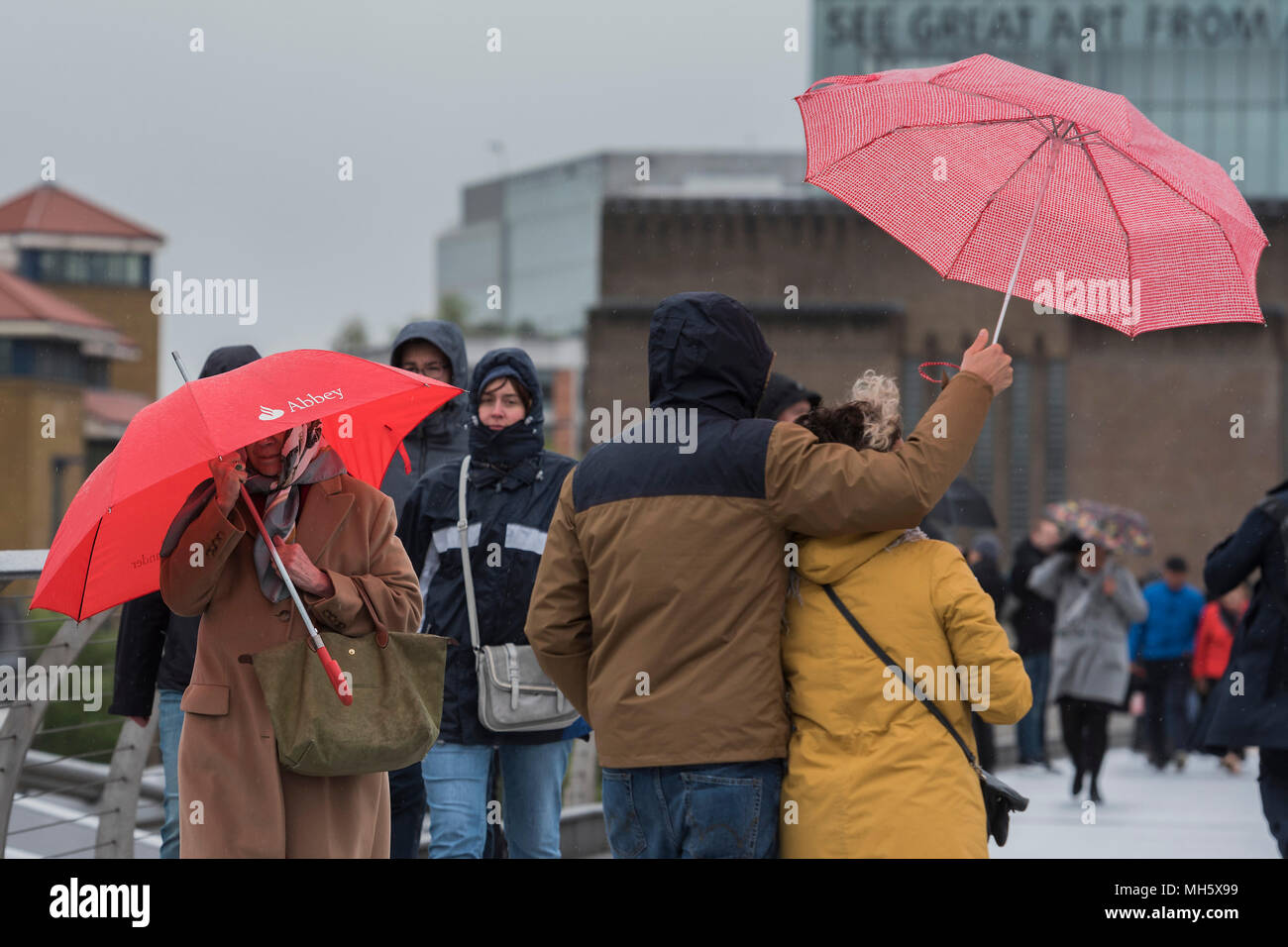 London, UK. 30th April 2018. People struggle with umbrellas as they cross the Millenniium Bridge in the wind and rain. Credit: Guy Bell/Alamy Live News Stock Photo