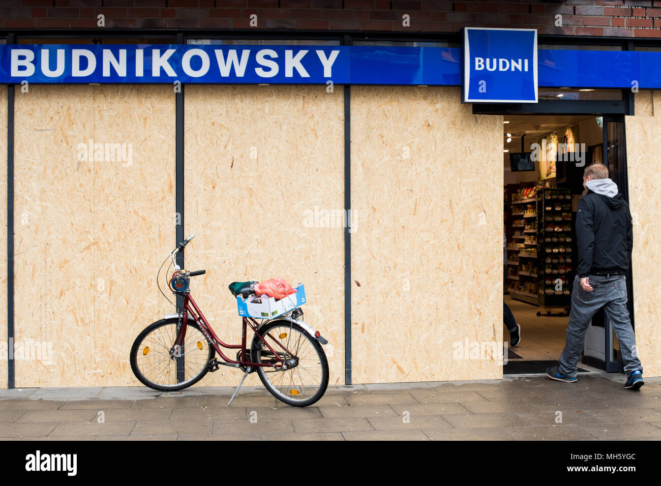 30 April 2018, Germany, Hamburg: A man enters a drug store that protected its windows with boards. In the last years, again and again there were riots in the course of the 1st of May demonstrations in Hamburg. Photo: Malte Christians/dpa Stock Photo