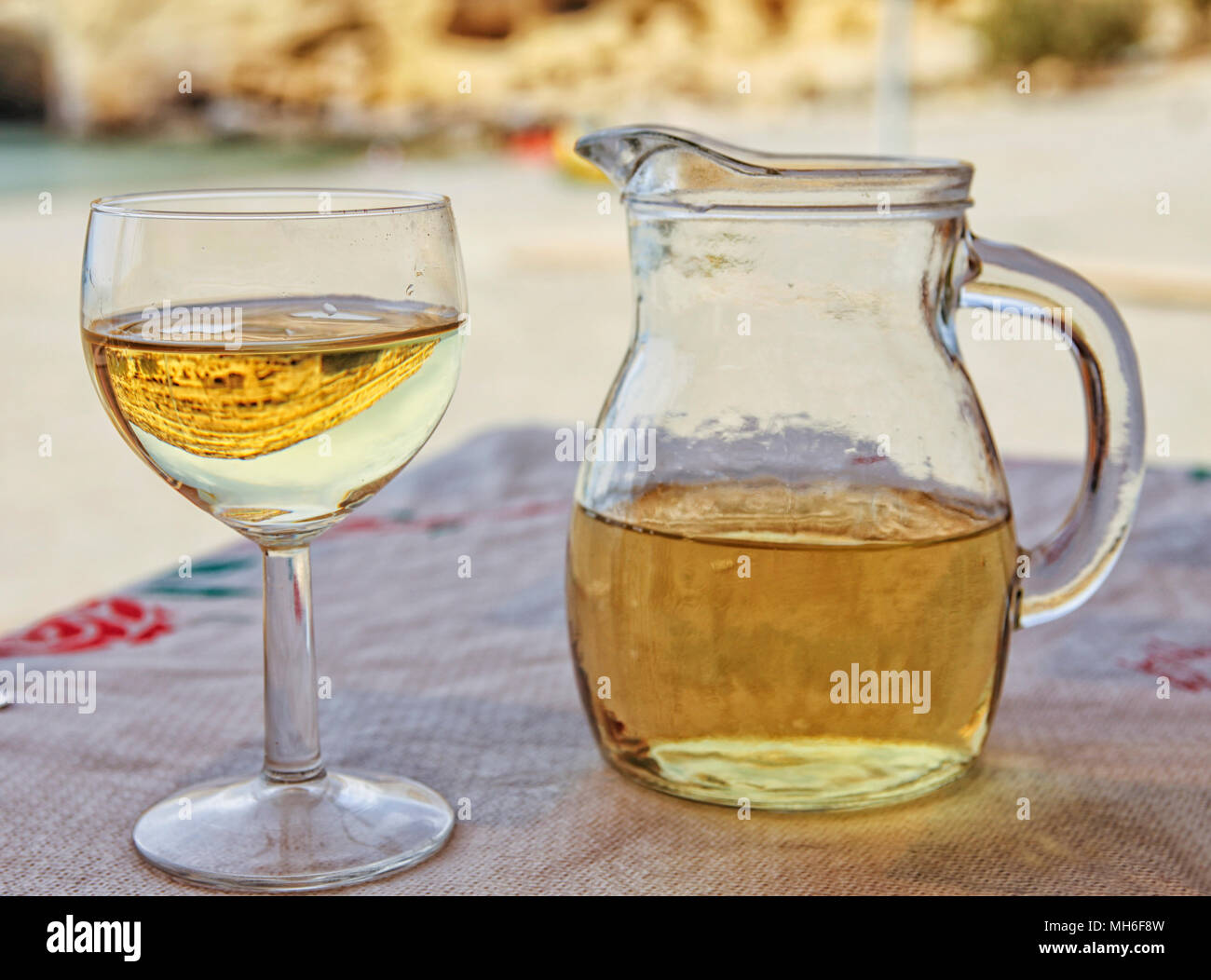 White wine with carafe on restaurant table in Crete. You can see the reflection of the famous Matala caves in the glass Stock Photo