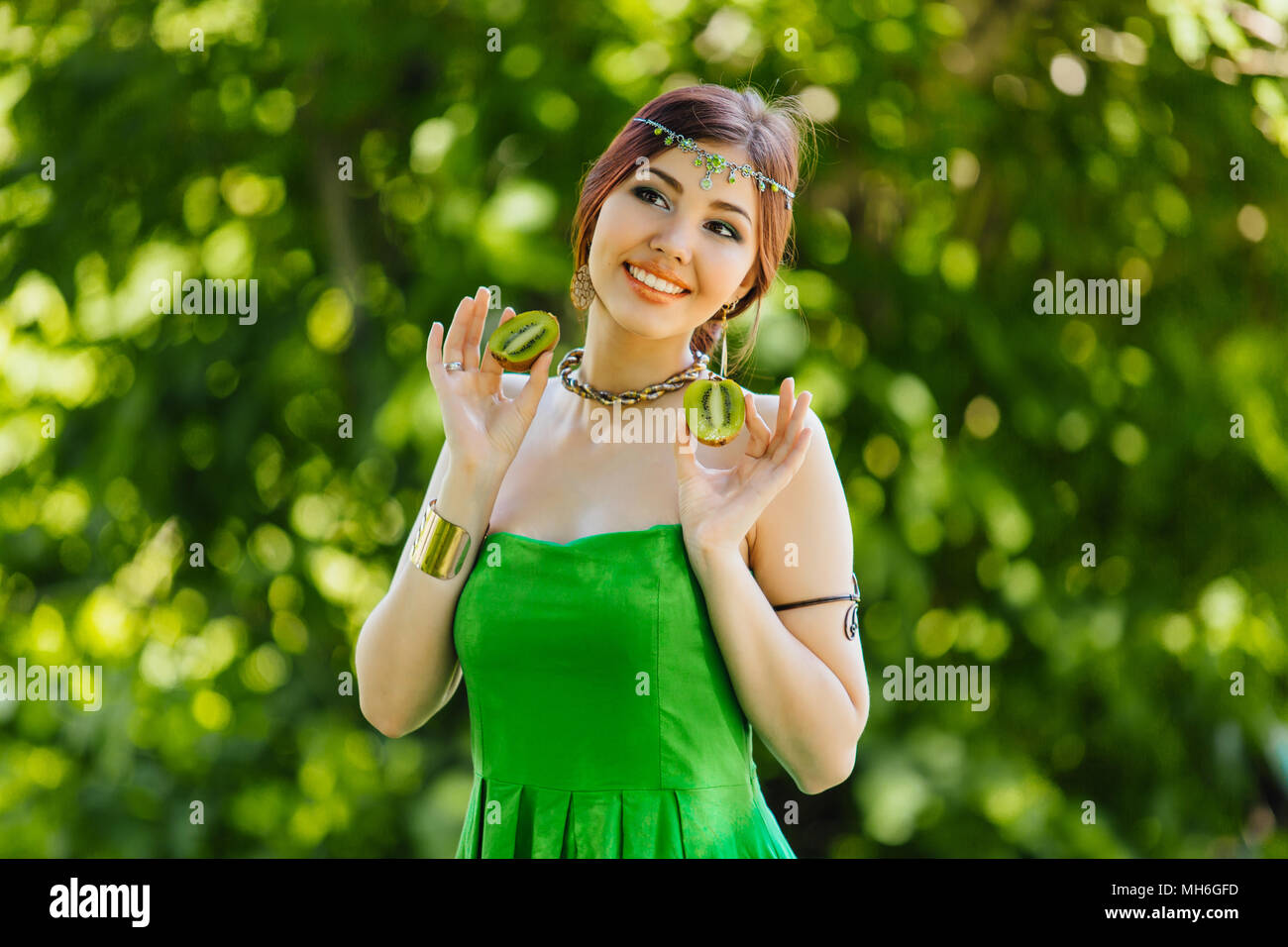 Portrait of a beautiful young asian woman holding two halves of kiwi ...
