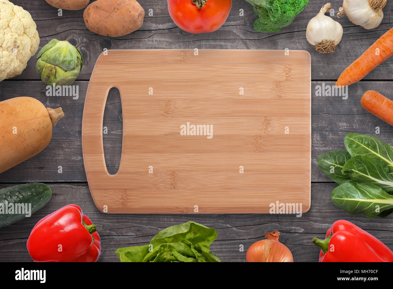 Food cutting board surrounded with vegetables on black wooden desk. Vintage, flat lay, top view. Stock Photo