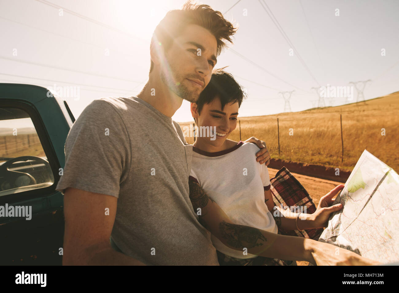 Couple looking at a map for navigation while on a road trip. Woman pointing at the map while the man looks away in the country side. Stock Photo