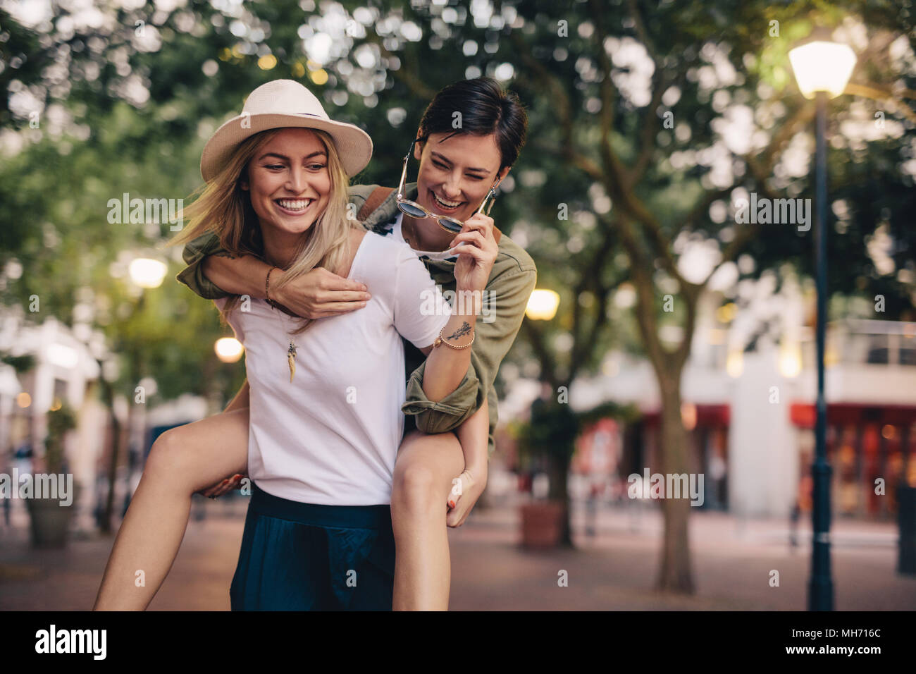 Outdoor shot of female friends walking outdoors in city and having fun. Two young women piggybacking and enjoying. Stock Photo
