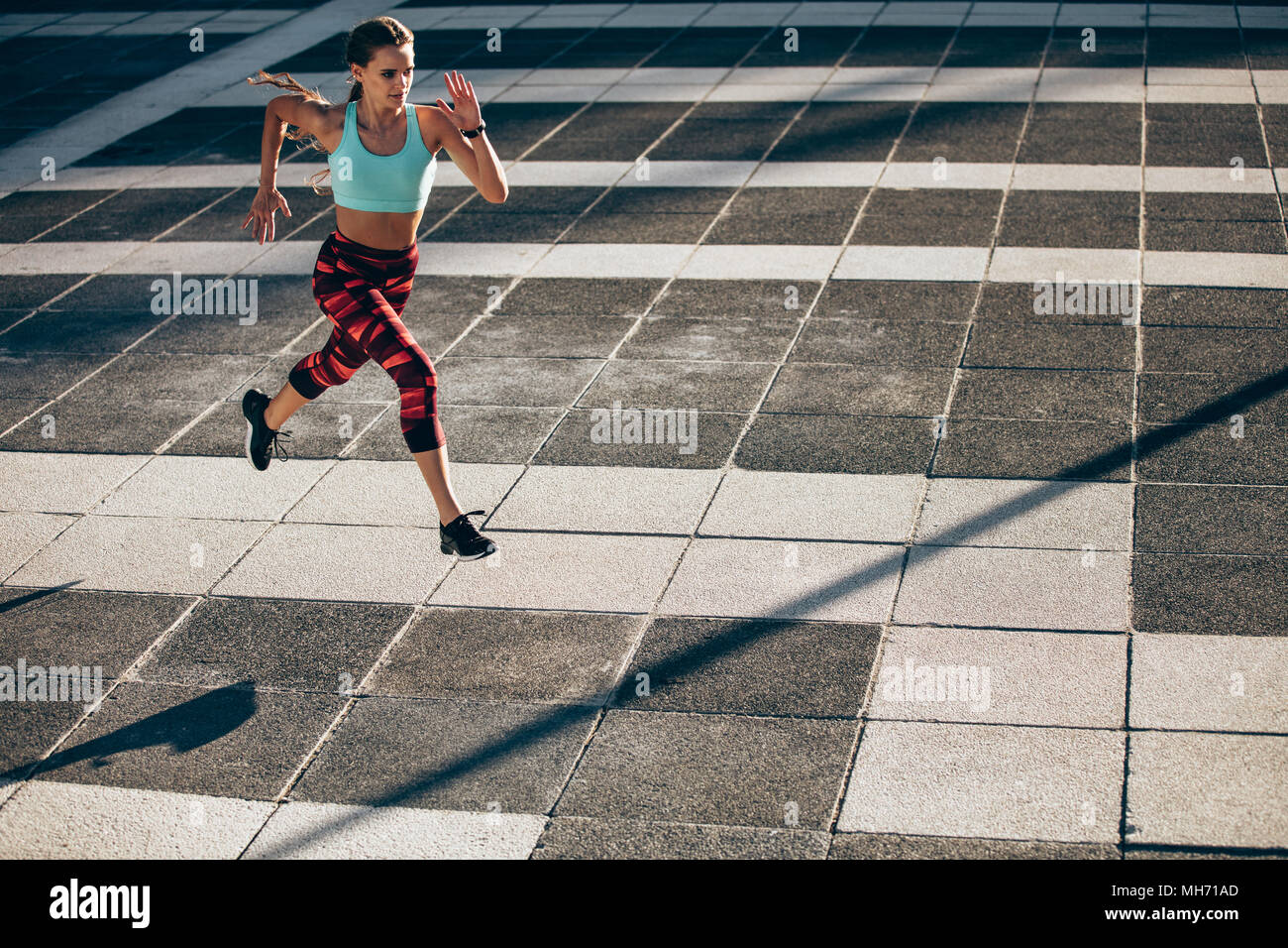 Sports woman in running and jumping outdoors in the city. Female athlete in running attire exercising in morning. Stock Photo