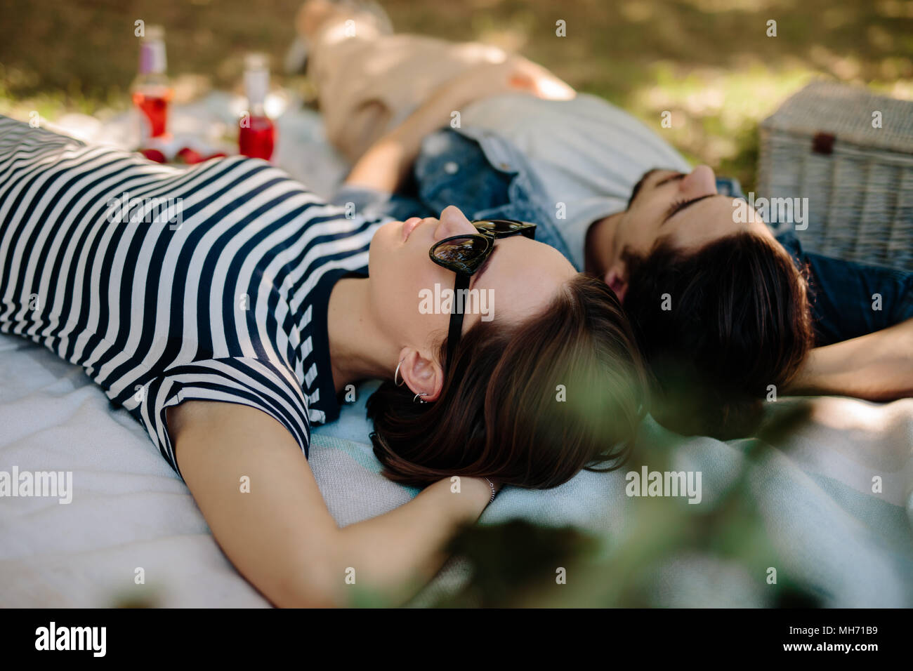 Beautiful woman wearing sunglasses lying down on a blanket with her boyfriend. Couple relaxing at a park during picnic. Stock Photo