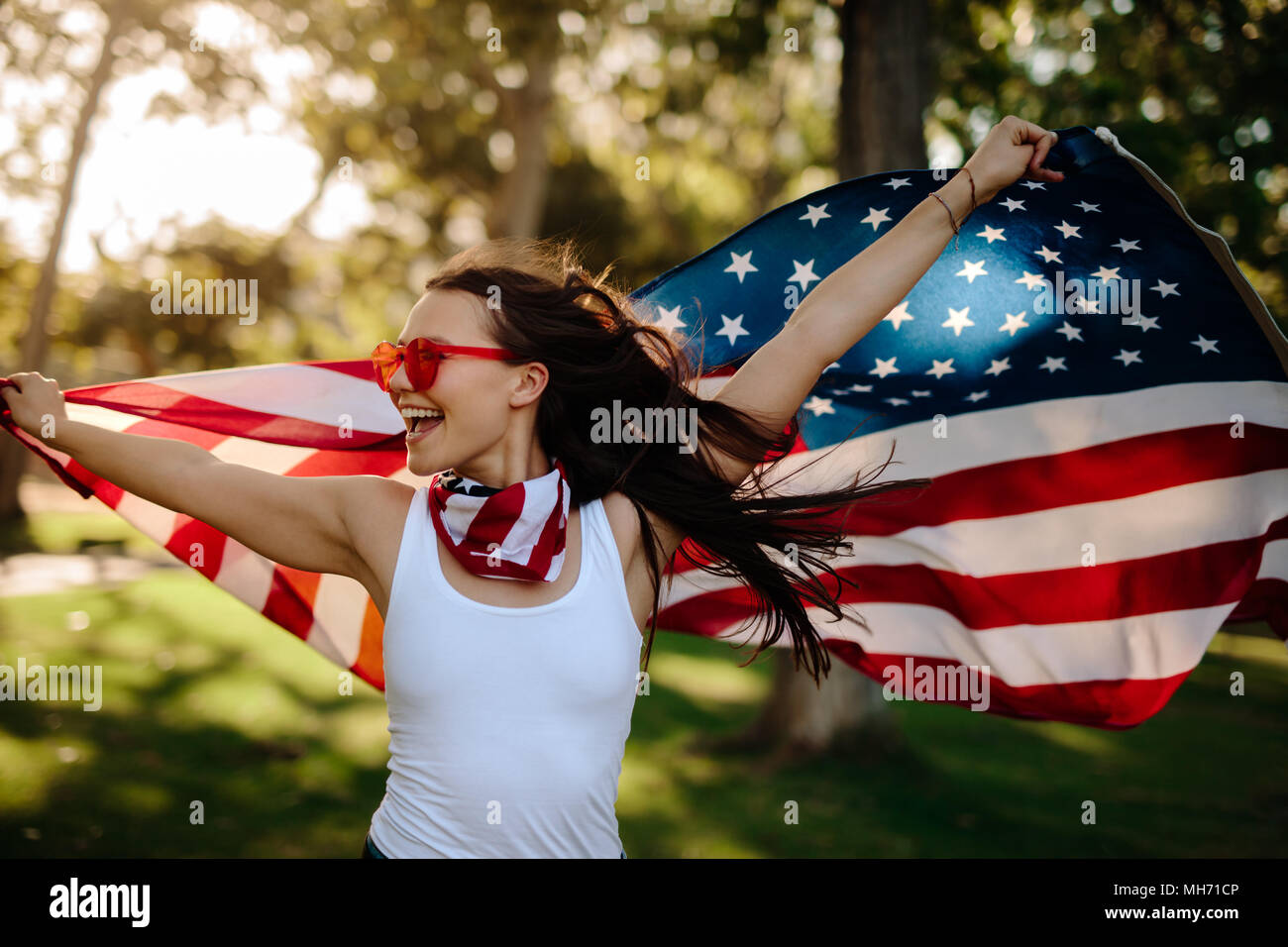 Young woman enjoying in park holding USA flag. American girl with national flag having fun at the park. Stock Photo