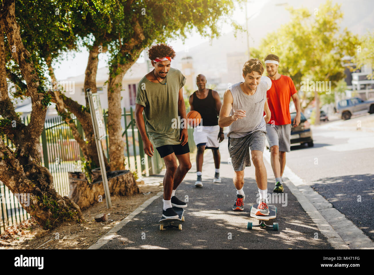 Two men skating on skateboard on a pavement while their mates cheer
