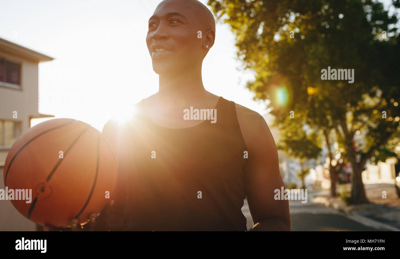 Close up of an athlete standing on street holding a basketball with sun in the background. Stock Photo