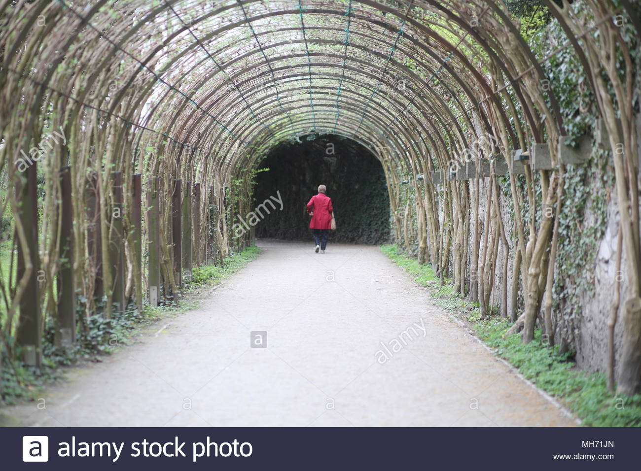 A woman in a red coat walks through the Mirabell gardens in Salzburg, Austria. Stock Photo