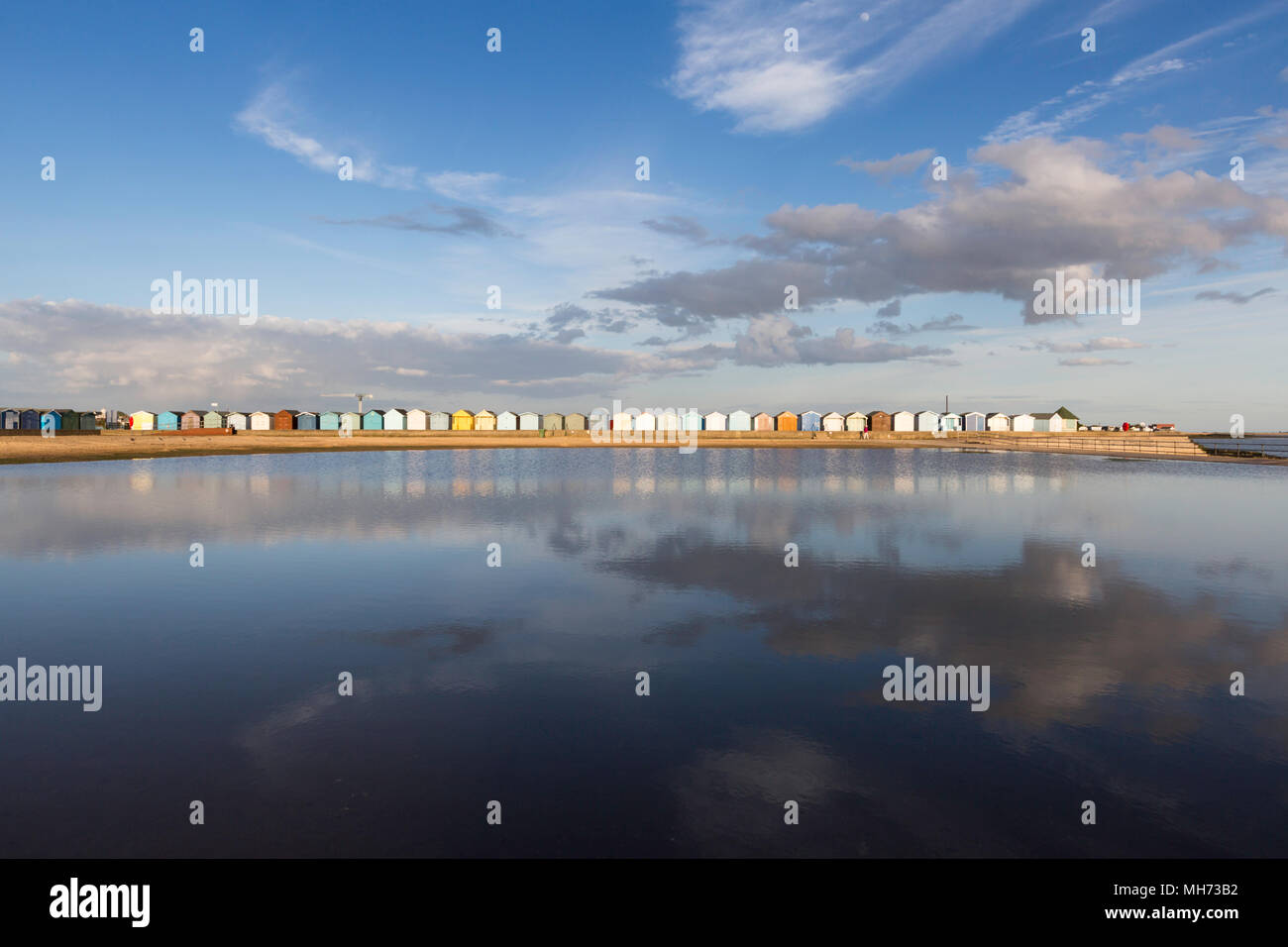 Dramatic cloudscape and the colourful beach huts reflected in the water of the tidal pool, Brightlingsea, Essex, UK. Stock Photo