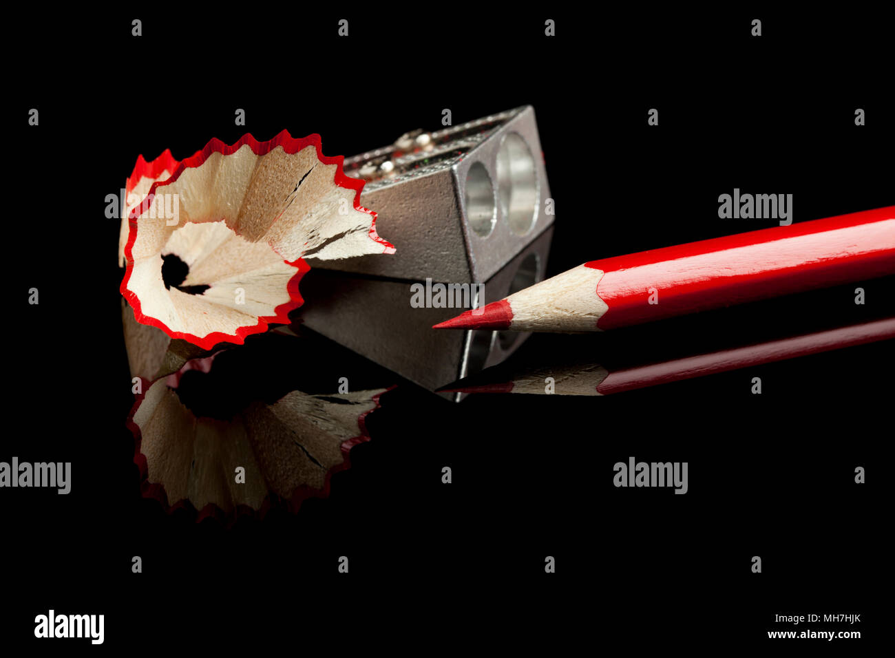 sharpened red pencil  with sharpener and shavings on reflective black surface Stock Photo
