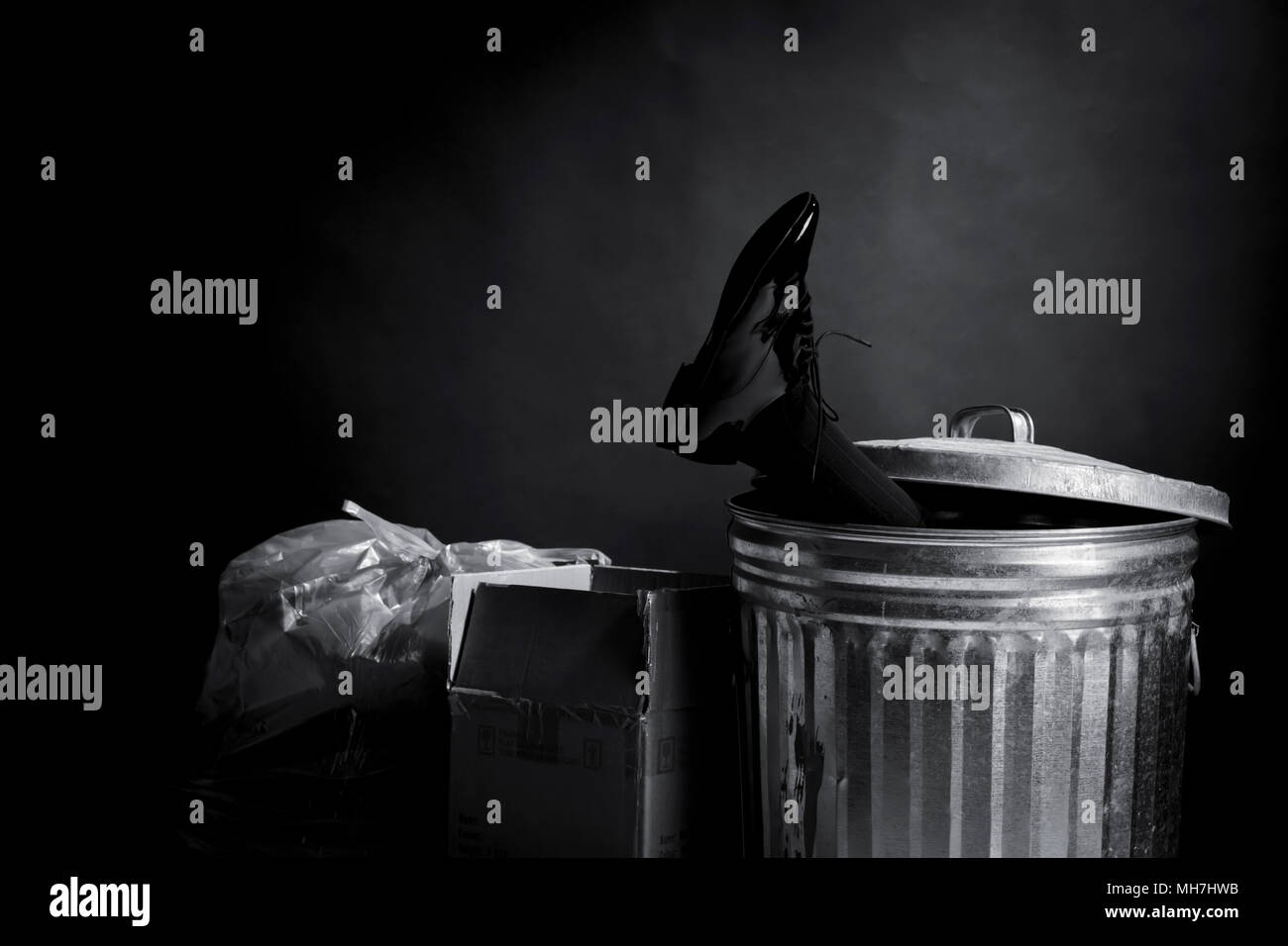 Foot of businessman with patent leather shoe sticking out of trash can Stock Photo