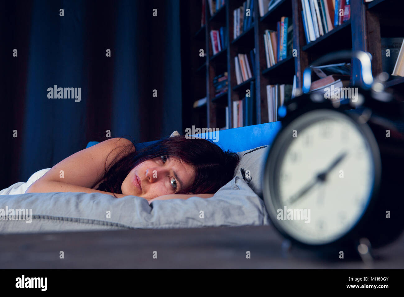 Photo of brunette with insomnia lying on bed next to alarm clock at night Stock Photo