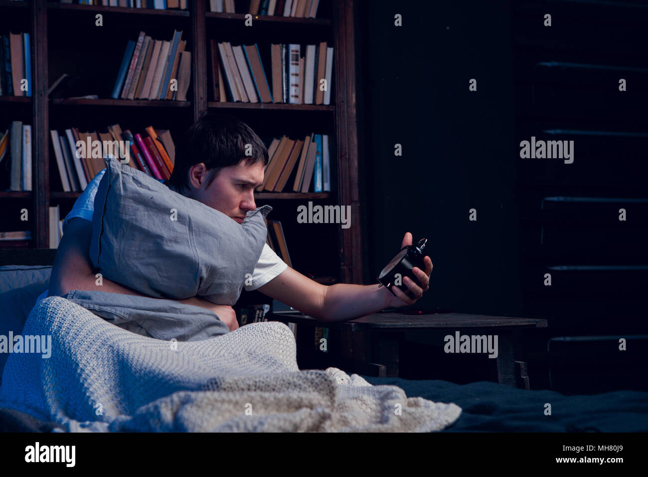 Image of man with insomnia sitting in bed with alarm clock Stock Photo