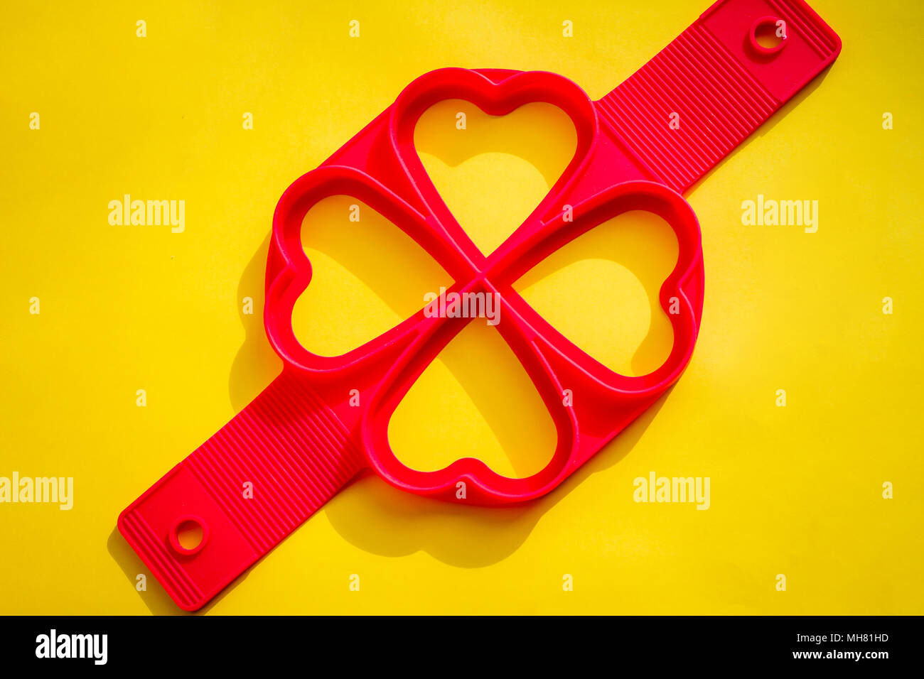 Red silicone mold on a yellow background.Silicone Heart Shape Egg Ring for Frying Pan.Frying egg with silicone form and teflon pan. molds for baking puncakes.bakery products Stock Photo