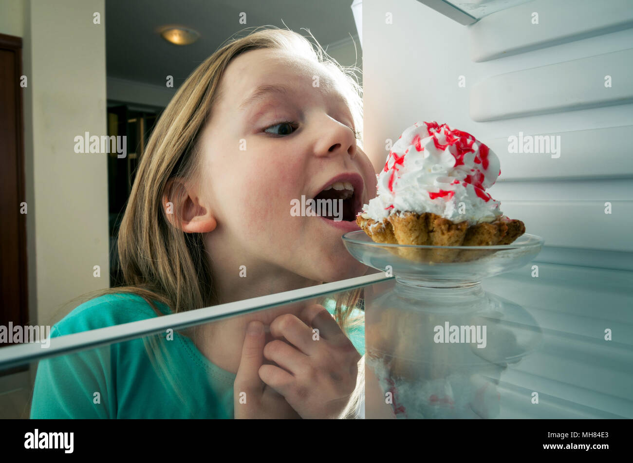 Small girl stealing the cake from fridge Stock Photo