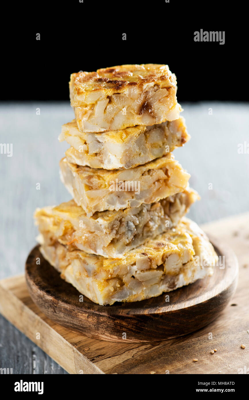 some pieces of typical tortilla de patatas, spanish omelet, on a rustic wooden table, against a black background Stock Photo