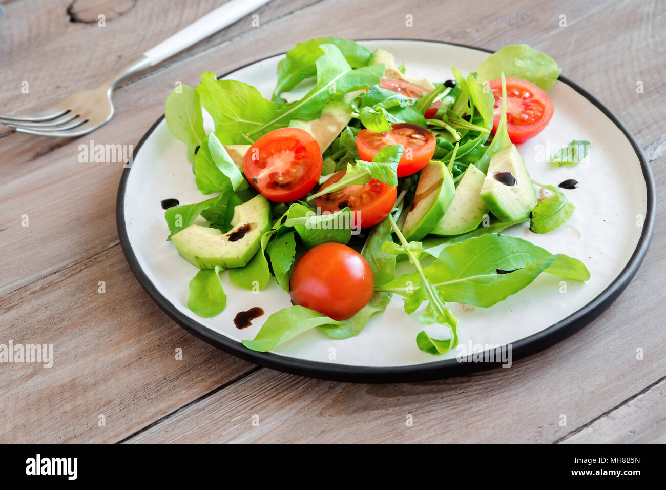 Avocado and tomatoes salad with arugula and balsamic vinegar over wooden, copy space. Healthy diet vegan vegetarian summer vegetable salad food concep Stock Photo