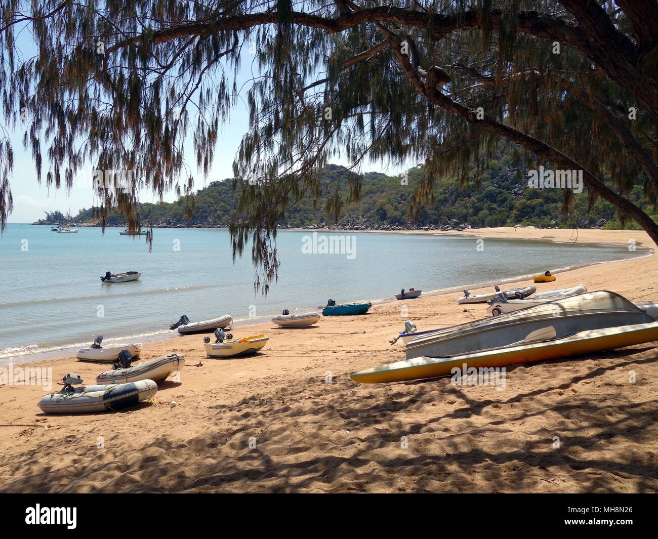 Magnetic Island, Queensland, Australia: August 31, 2017: Boats resting on a pretty sandy beach looking through trees on an island Stock Photo