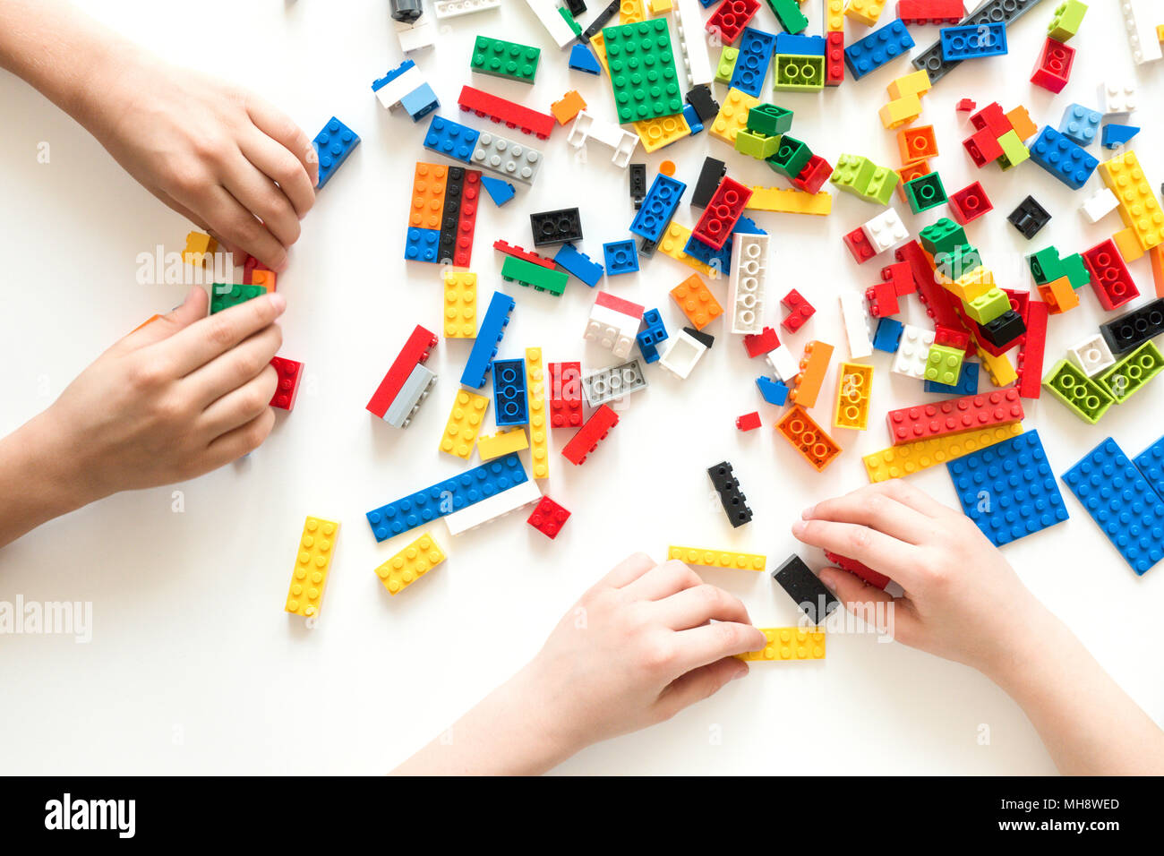 Children hands play with colorful lego blocks on white table. Stock Photo