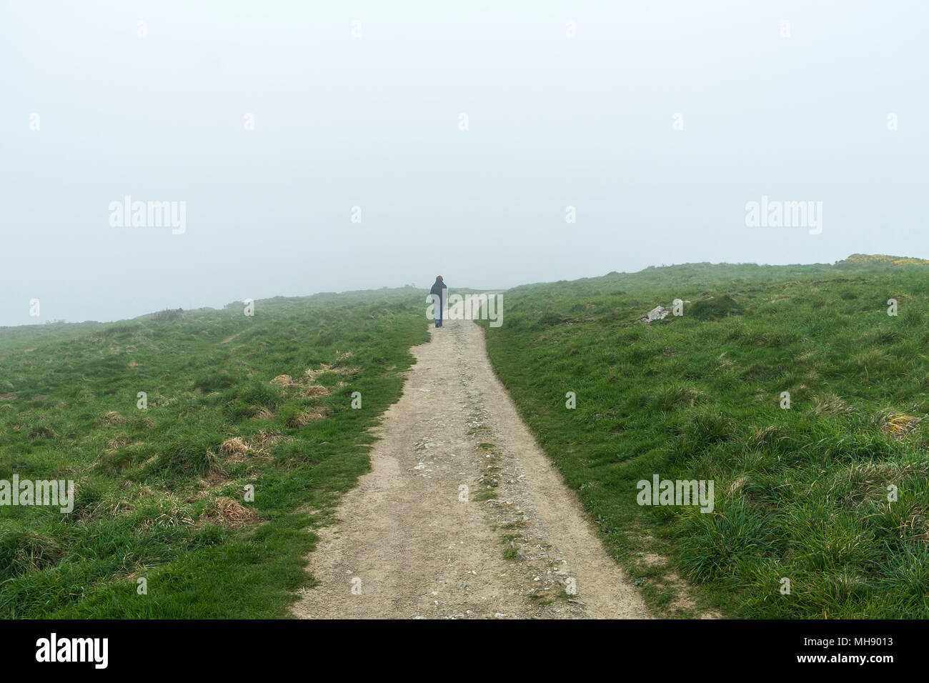 A woman walking alone along a coastal path track in misty conditions. Stock Photo