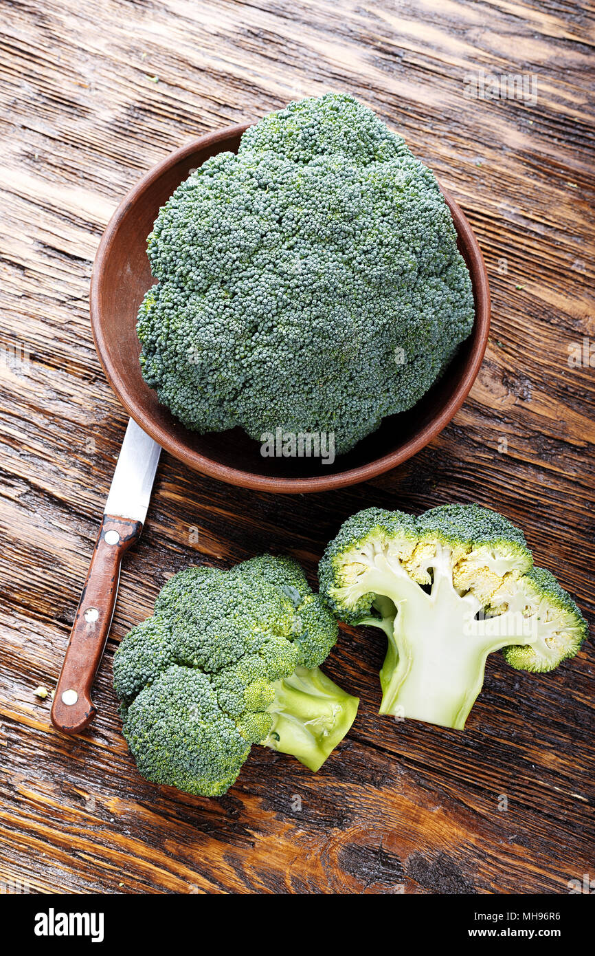 broccoli in a clay plate on a wooden table, next to a whole cabbage are ...