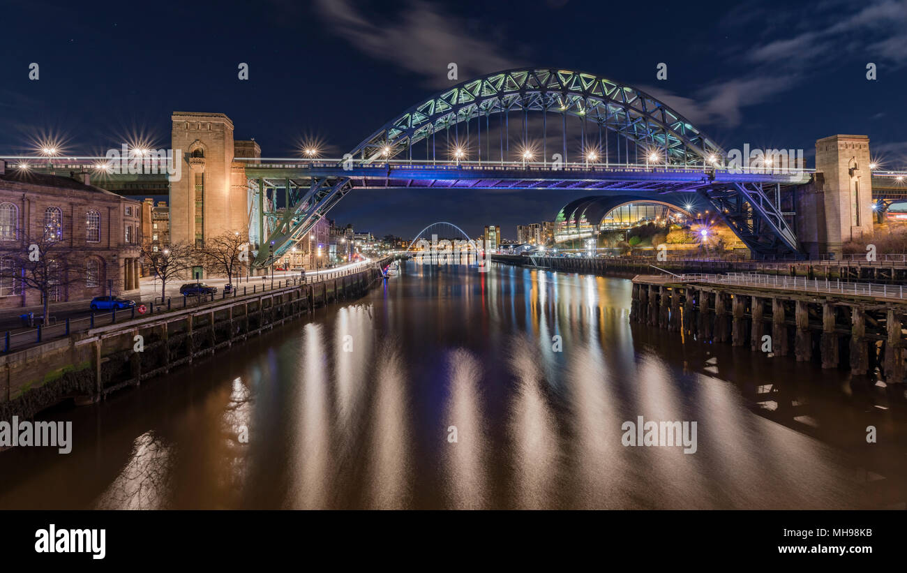 Spectacular views around Newcastle Quayside at night with the Millenium Bridge, Swing Bridge and Tyne bridge lit up and a blue sky behind Stock Photo