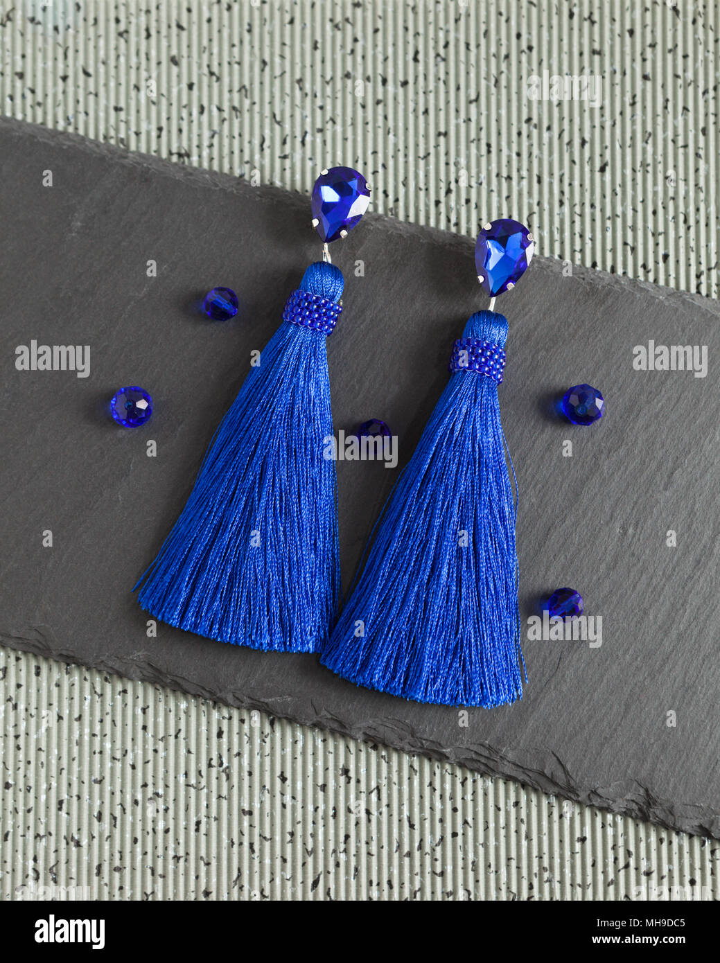 Blue beautiful handmade earrings with shiny crystals and tassels, lying flat on the grey stone background, top view Stock Photo