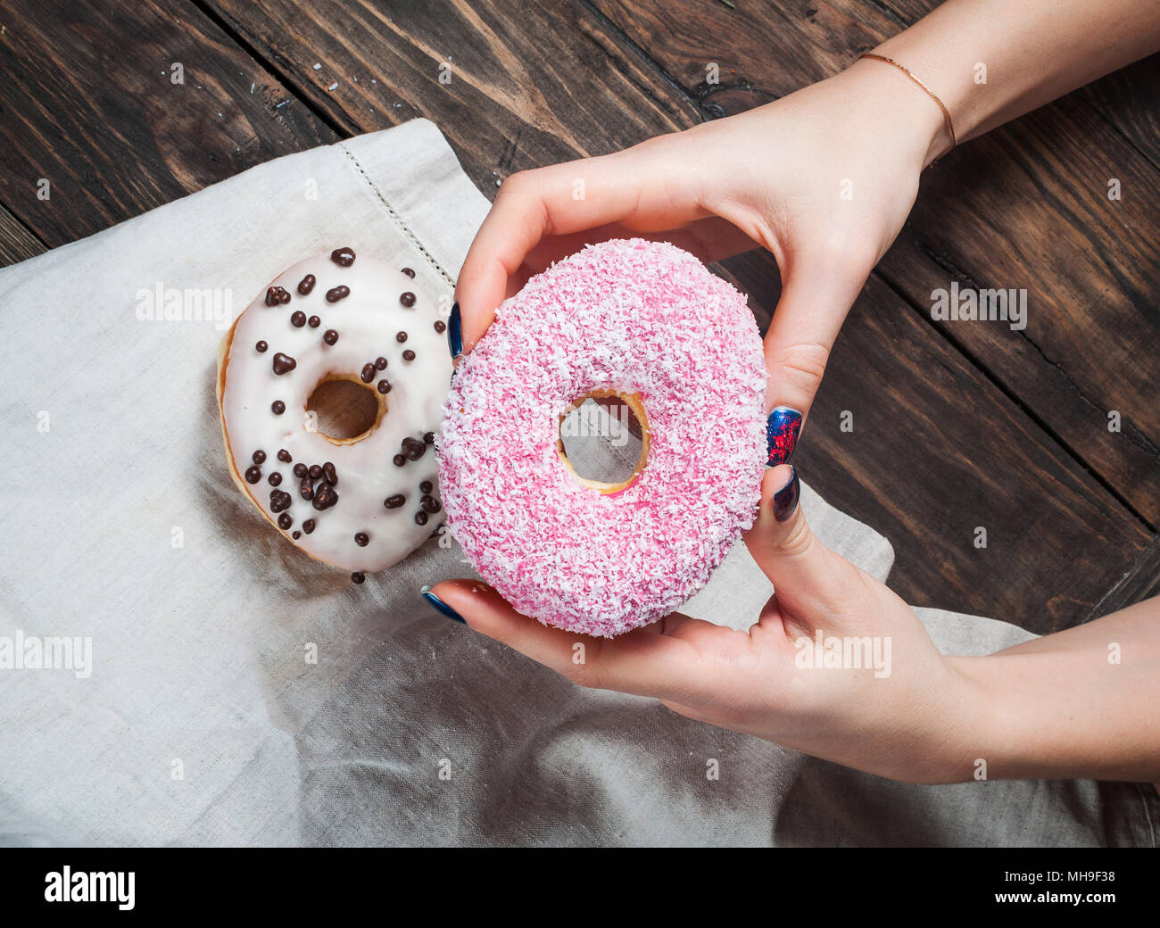 Female hand picking sweet sugary donut from rustic wooden kitchen table, tasty bakery doughnuts overhead shot, top view Stock Photo