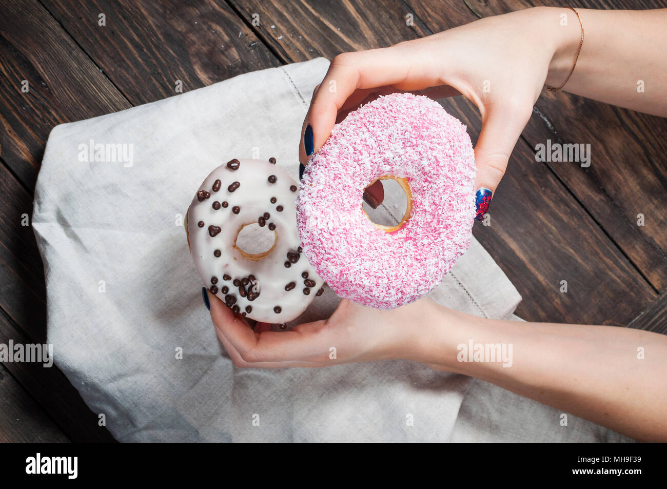 Female hand picking sweet sugary donut from rustic wooden kitchen table, tasty bakery doughnuts overhead shot, top view Stock Photo