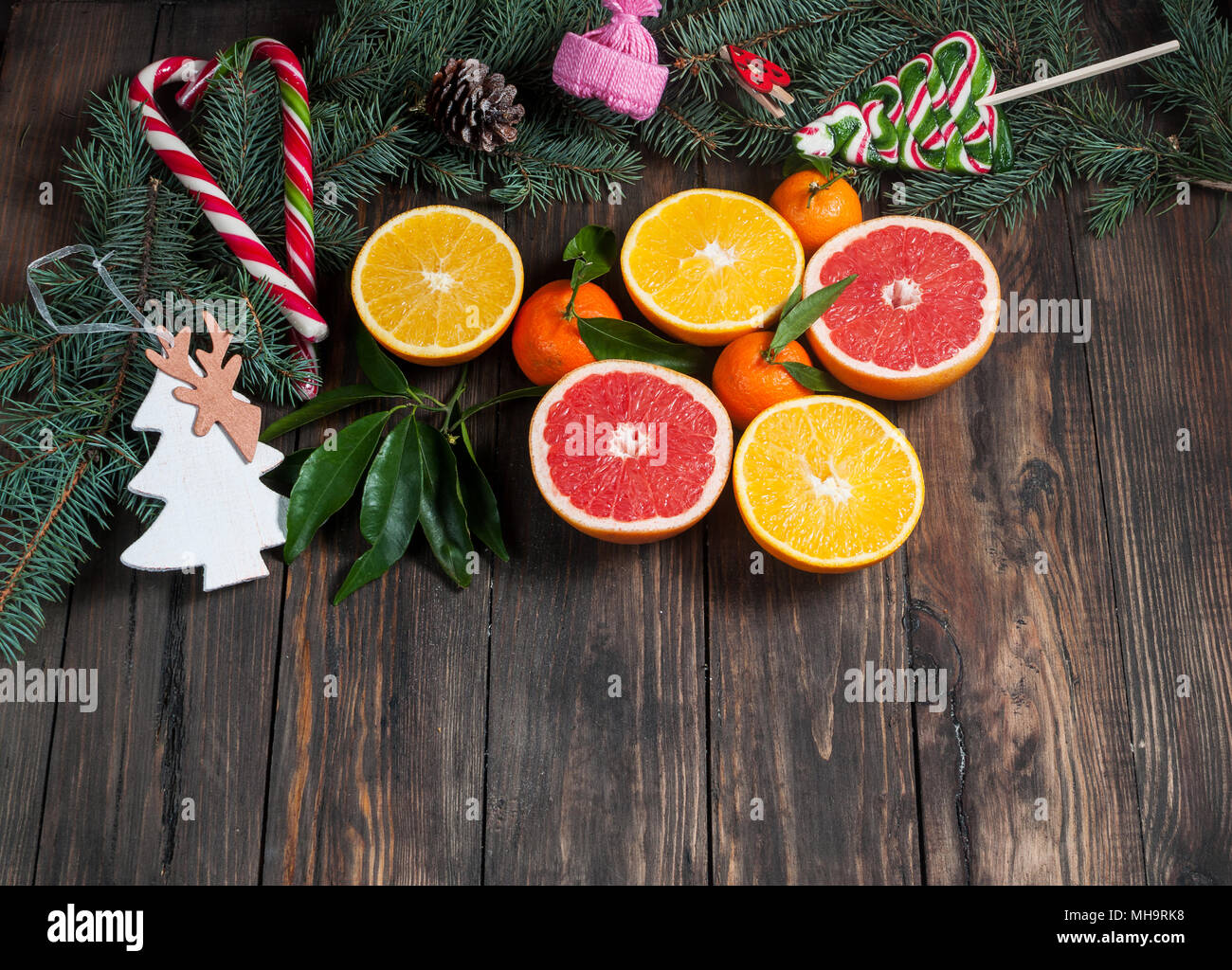 Tangerines with leaves in Christmas decor with Christmas tree, dry orange and candies over old wooden table. Rustic style. Top view Stock Photo