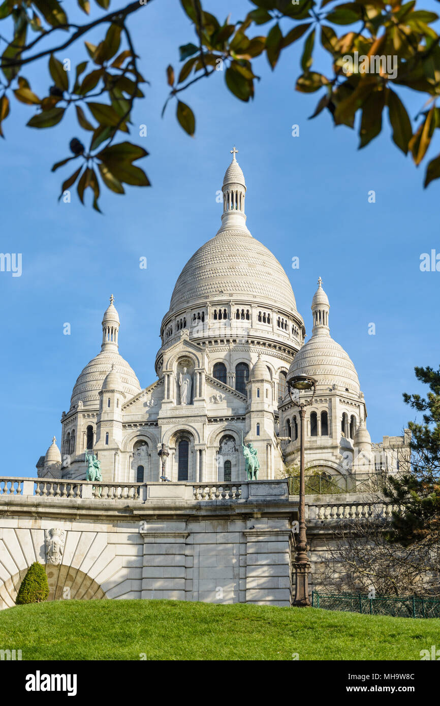 The basilica of the Sacred Heart of Paris at the top of the Montmartre hill seen from the Louise Michel park with foliage in the foreground. Stock Photo