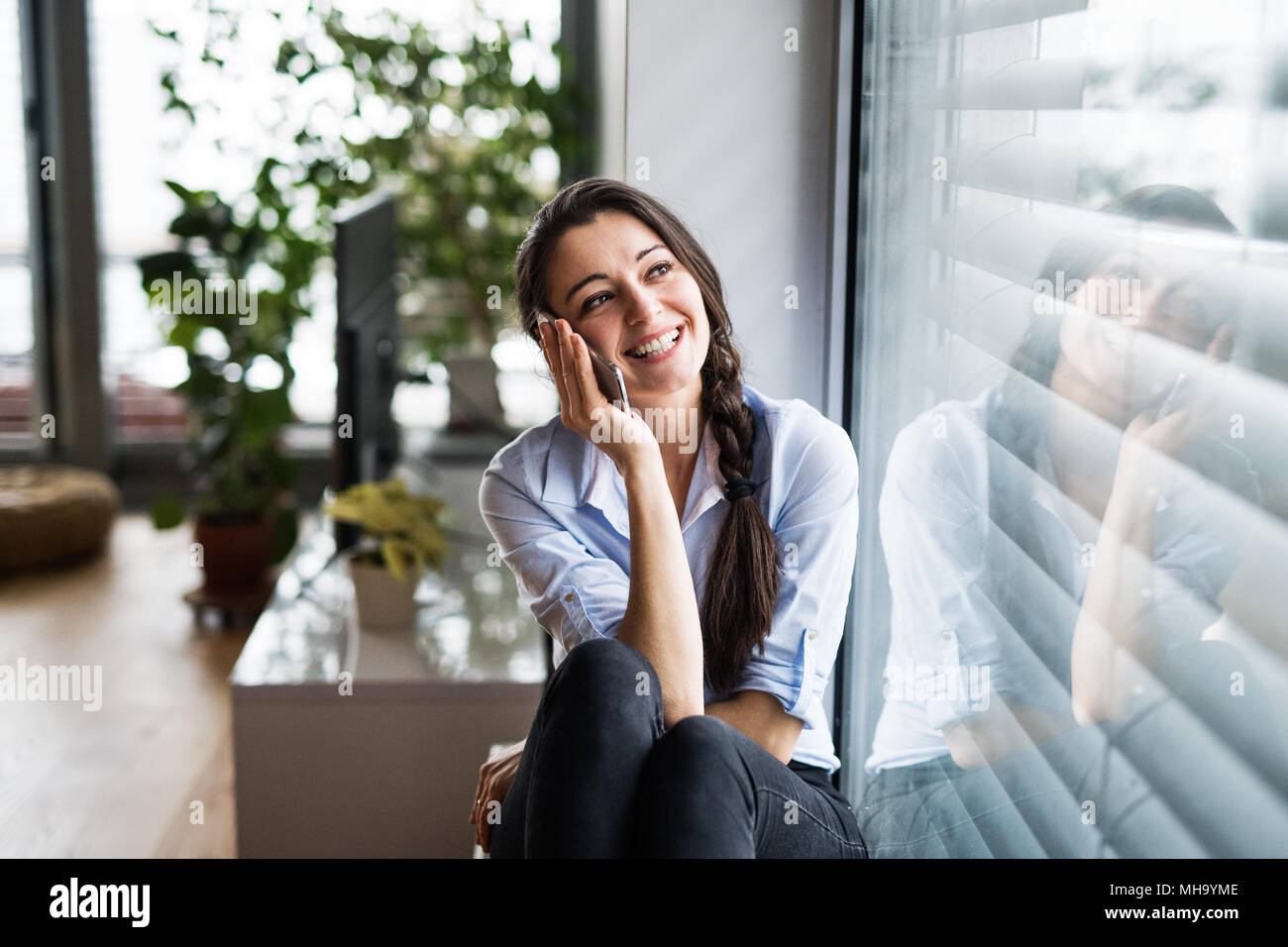 Woman with smartphone by the window at home, making a phone call Stock
