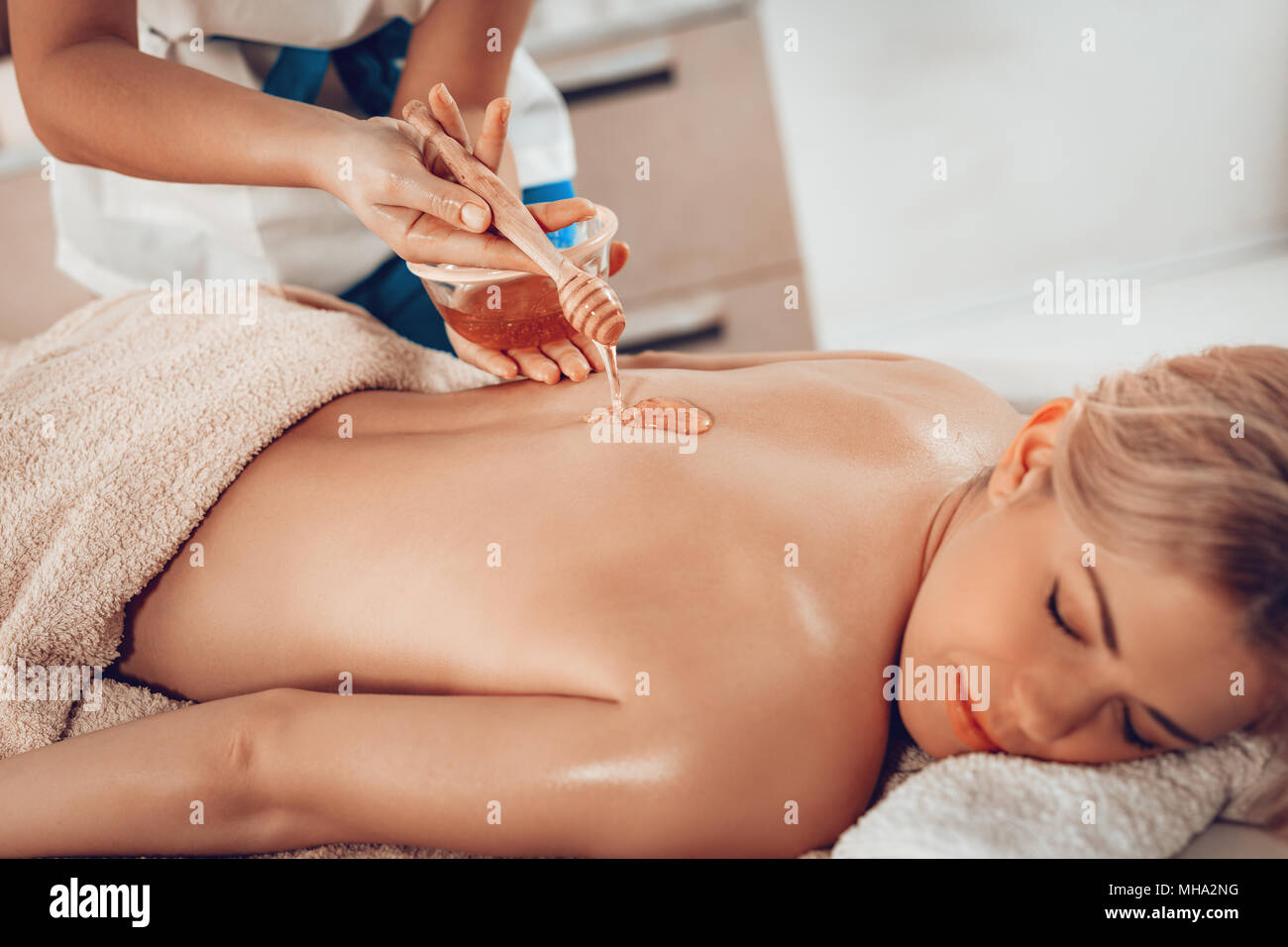 Beautiful young woman lying down and getting healthy back massage with honey by female therapist in the spa center. Stock Photo