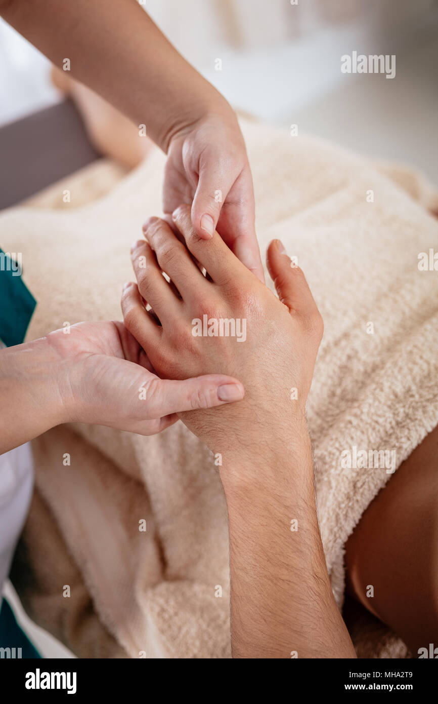 Close-up of a hads of young female therapist massaging young man's hand at beauty salon. Stock Photo